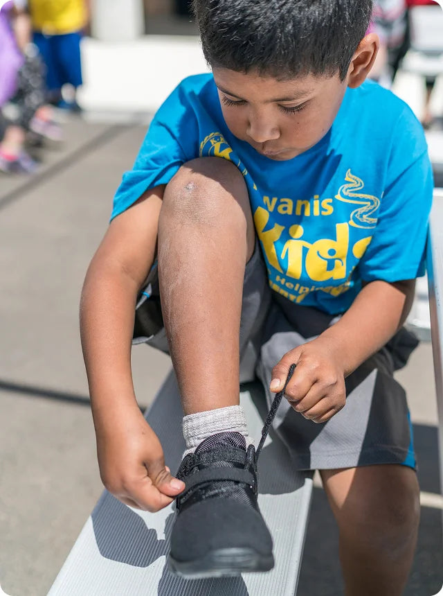 A kid from Save the Children tying his shoes.