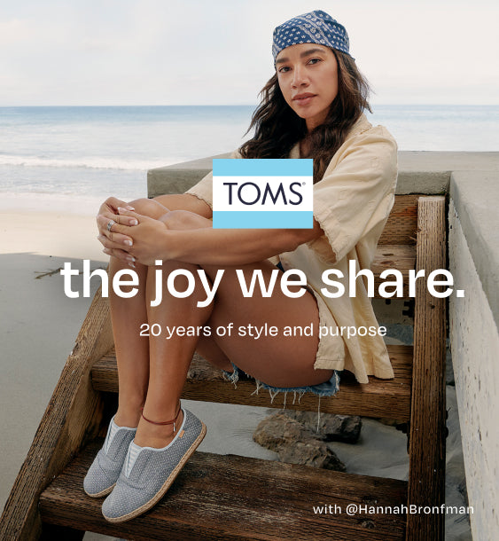 TOMS logo. the joy we share. Celebrating 20 years of style and purpose with tastemaker Hannah Bronfman and family. Shop the Anniversary Collection. Caption: with @HannahBronfman. Hannah sitting. Beach background.