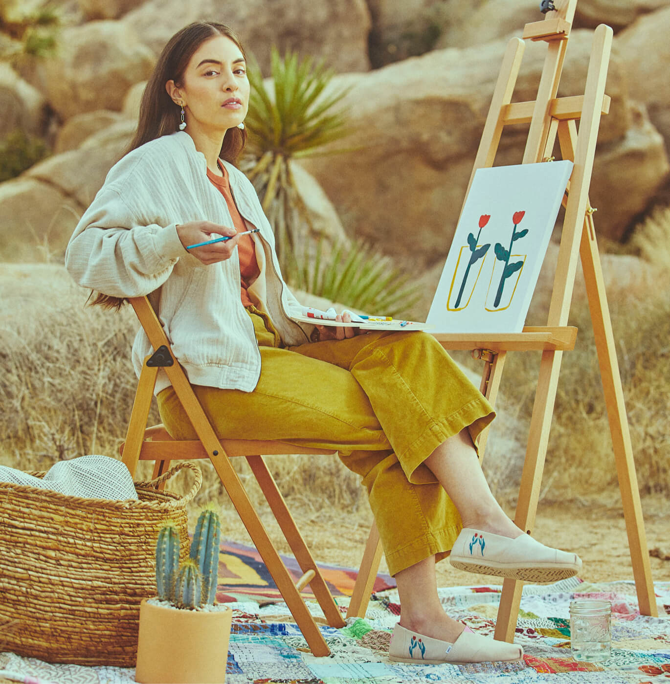 Illustrator Ludi Leiva sitting at her easel painting and wearing the TOMS X Ludi Leiva Alpargata in Natural.